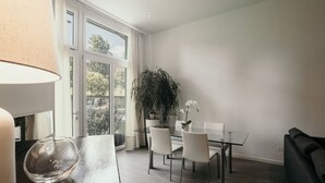 A modern dining area with a glass table, white chairs, a large potted plant, and a sofa. - GuestHost - Studio 1 is the best you could wish for in Bologna, a comfortable and beautiful home. It's a spacious, renovated and stylishly furnished two-room apartment, bright and airy, perfect for a couple or four friends. It's close to the highway and  (Bologna)