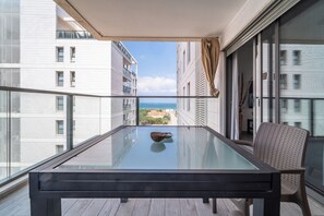 Een balkon met een glazen tafel en stoel, met uitzicht op een stadsbeeld en de zee.