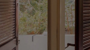 A room with a window, wooden shutters, and a view of trees and a fence. - Beach Haven 3BR Apt by Sea N' Rent (Nahariya)