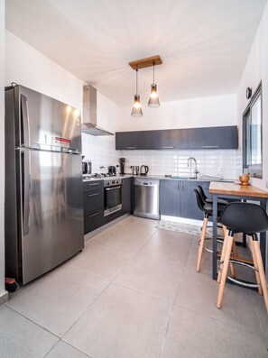 Cozinha moderna com eletrodomésticos de aço inoxidável, máquina de lavar louça e área de refeições com mesa de madeira e cadeiras pretas.