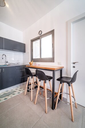 Uma cozinha moderna com área de refeições, destacando uma mesa de madeira, cadeiras pretas e uma janela com relógio.