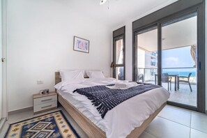 A bedroom with a bed, a nightstand, a window, and a view of the sea. - Beach Haven 3BR Apt by Sea N' Rent (Nahariya)