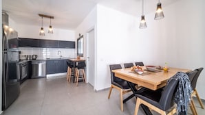 A modern kitchen with stainless steel appliances, black cabinets, and a wooden dining table with black chairs. - Beach Haven 3BR Apt by Sea N' Rent (Nahariya)