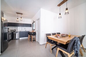 A modern kitchen with stainless steel appliances, a dining area with a wooden table and black chairs, and pendant lighting. - Beach Haven 3BR Apt by Sea N' Rent (Nahariya)