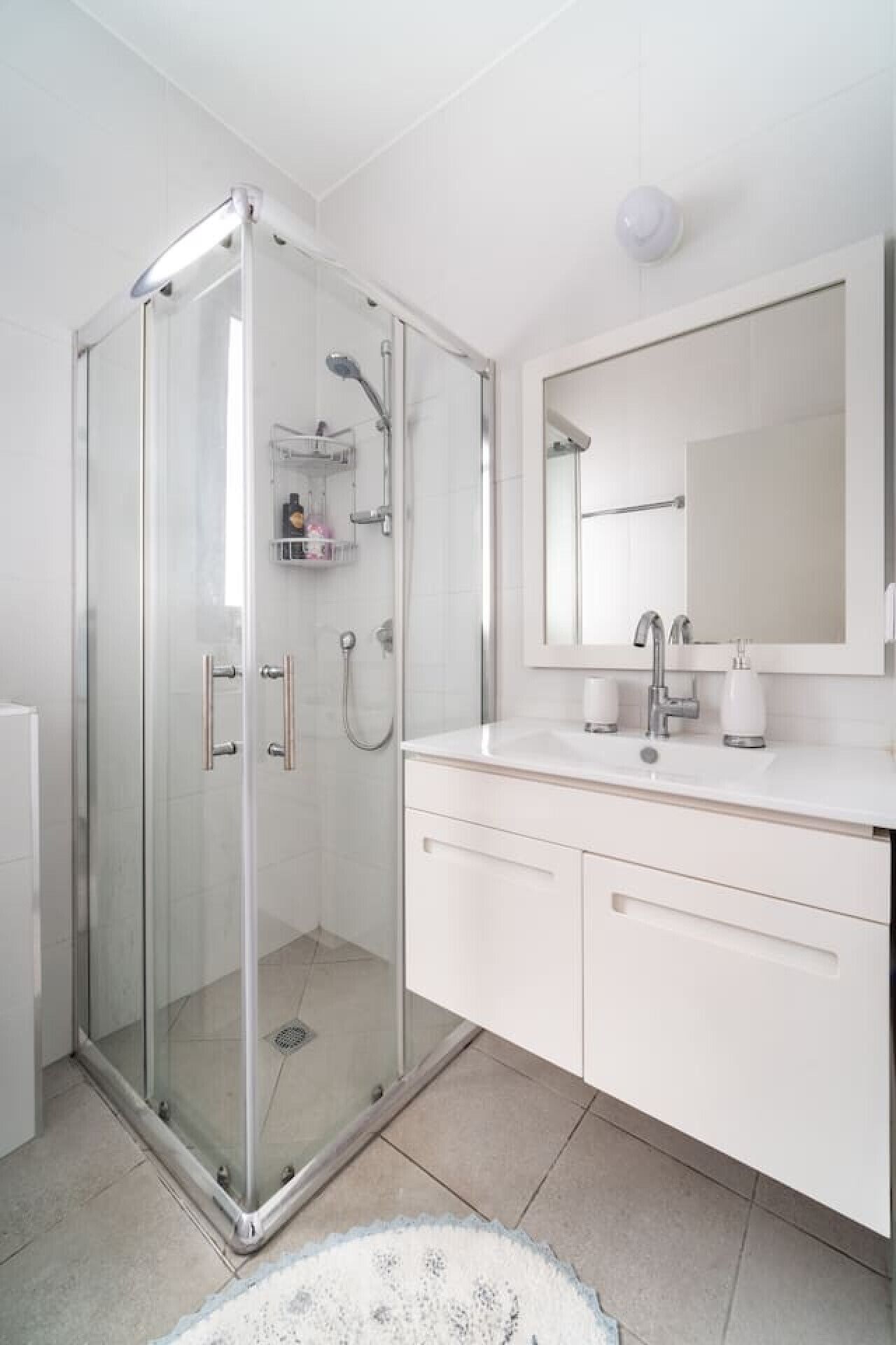 A modern bathroom with a glass-enclosed shower, a white vanity with a mirror, and a tiled floor.