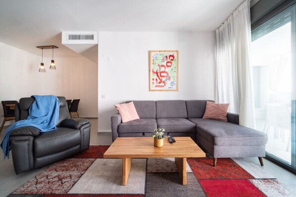 Een moderne woonkamer met een grijze hoekbank, een houten salontafel en een tapijt met een rood-wit patroon.