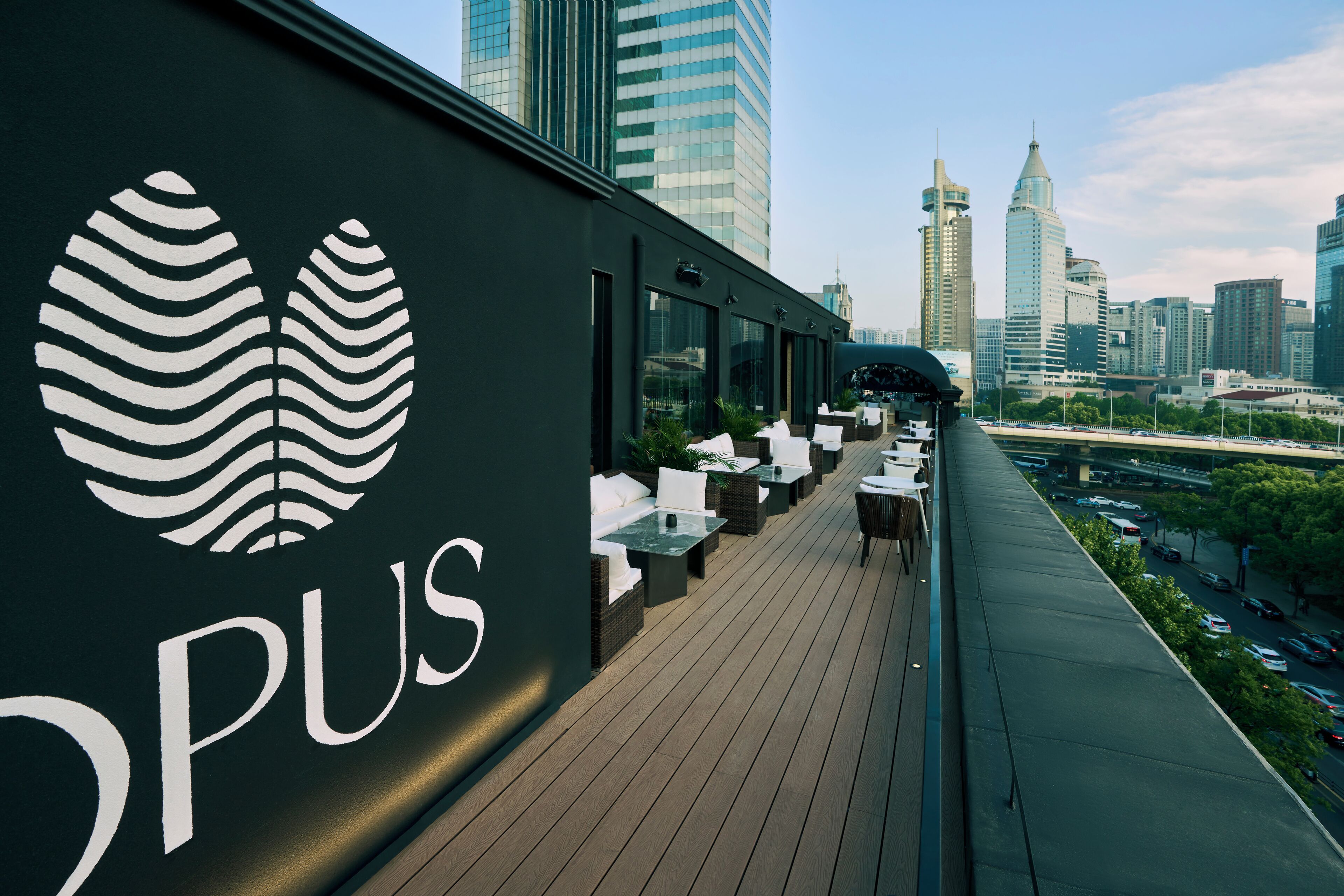 A rooftop bar with a city skyline view, featuring a modern design with a logo and outdoor seating.