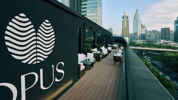 A rooftop bar with a city skyline view, featuring a modern design with a logo and outdoor seating.