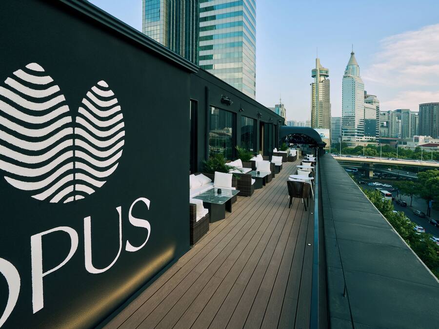 A rooftop bar with a city skyline view, featuring a modern design with a logo and outdoor seating.