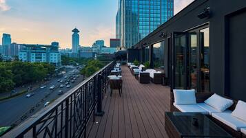 A rooftop terrace with outdoor seating, a city view, and a modern building in the background.