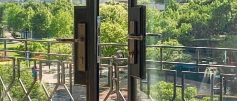 A view through a window of a cityscape with modern buildings, a park with trees, and a pedestrian walkway.