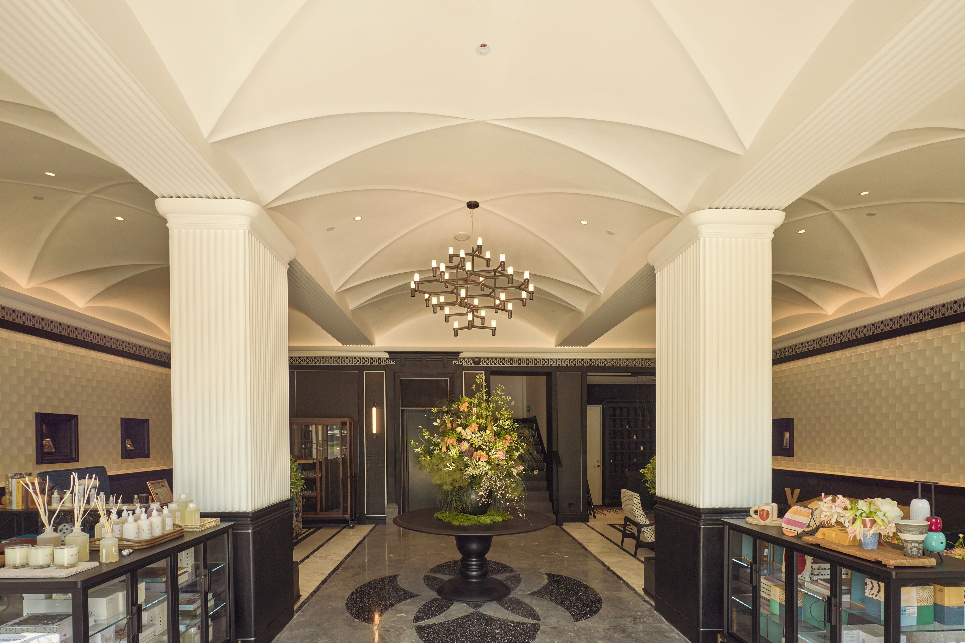 A lobby with a central floral arrangement, high ceilings, and a chandelier.