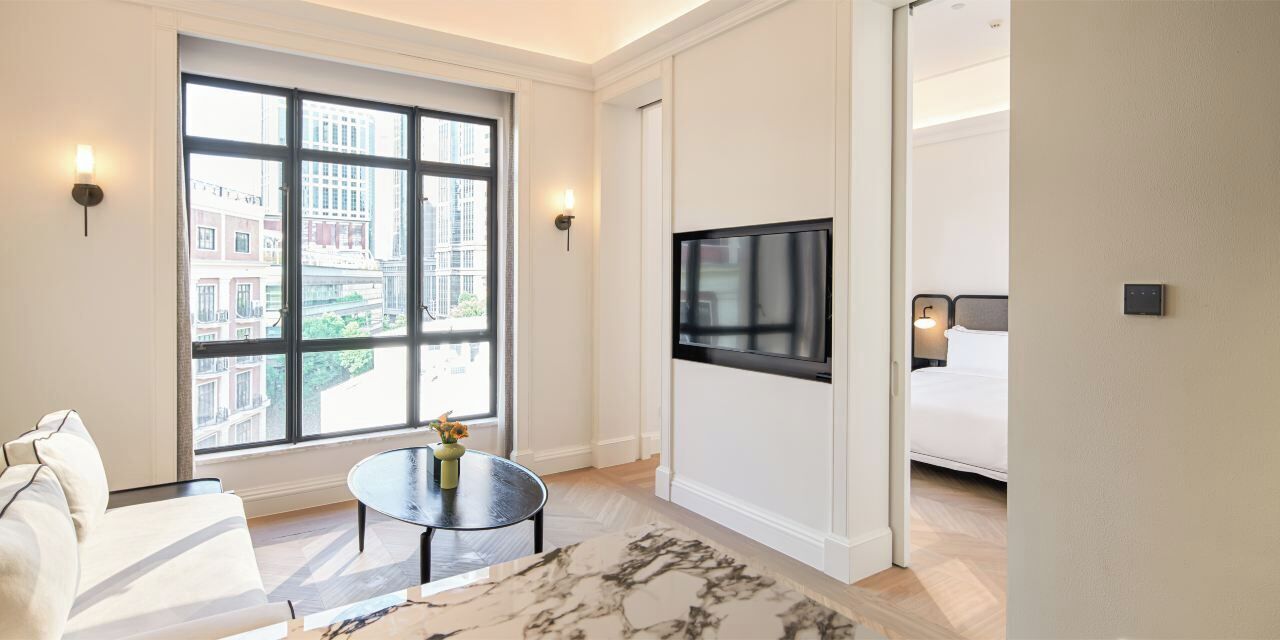 A hotel room with a large window, a flat-screen TV, a sofa, and a small table with a vase.