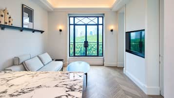 A modern living room with a marble coffee table, a sofa, a TV mounted on the wall, and a large window with a city view.