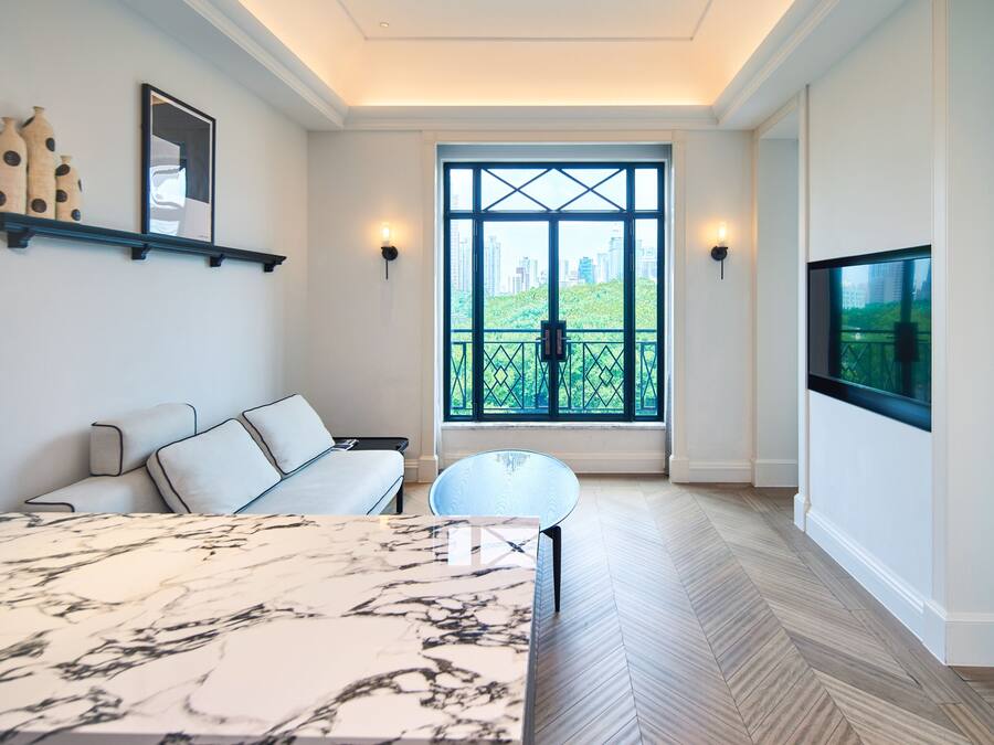A modern living room with a marble coffee table, a sofa, a TV mounted on the wall, and a large window with a city view.