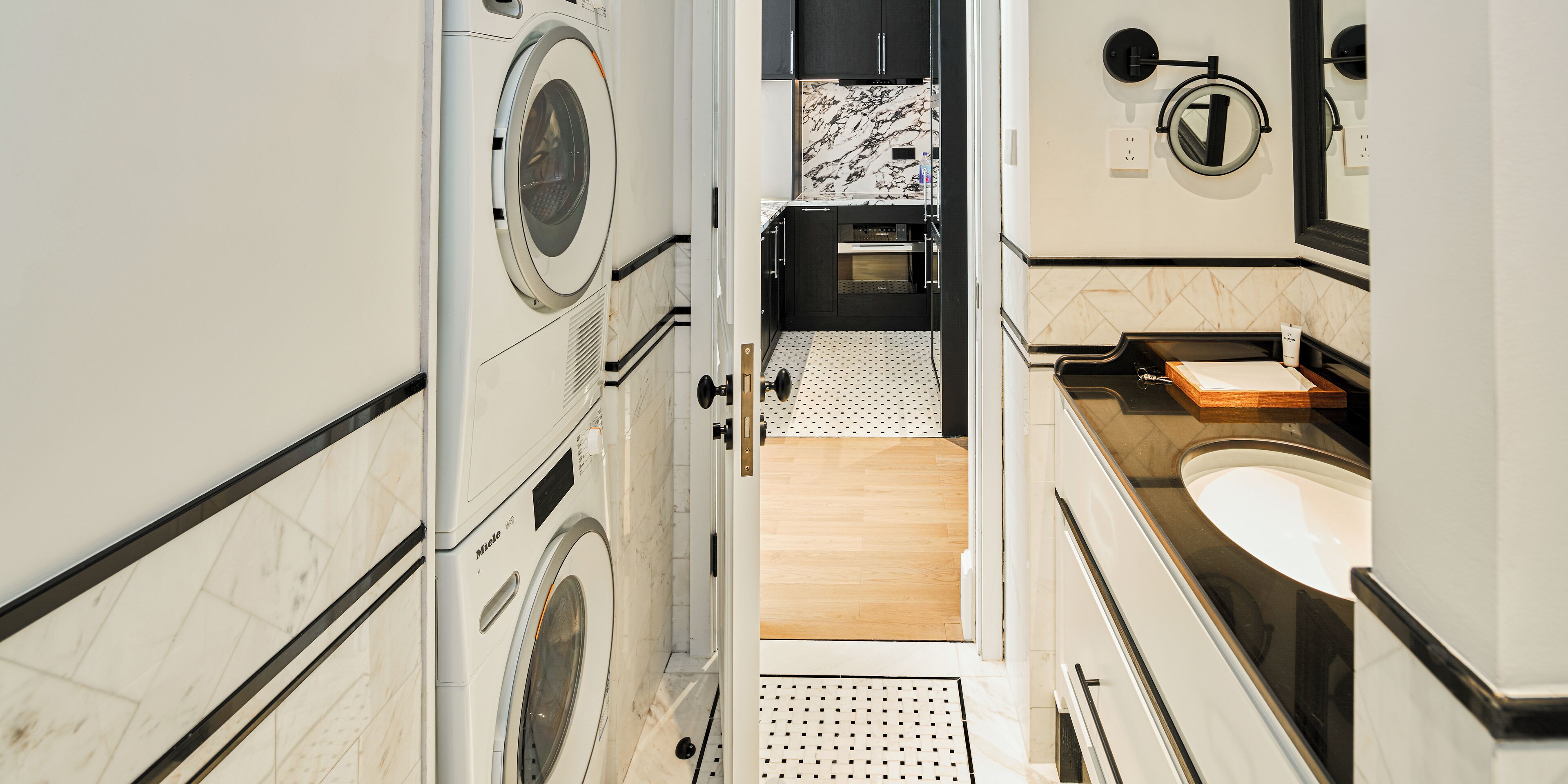 A compact hotel bathroom with a washing machine, a sink, and a mirror.