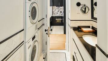 A compact hotel bathroom with a washing machine, a sink, and a mirror.
