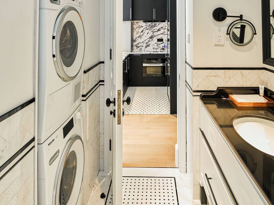 A compact hotel bathroom with a washing machine, a sink, and a mirror.