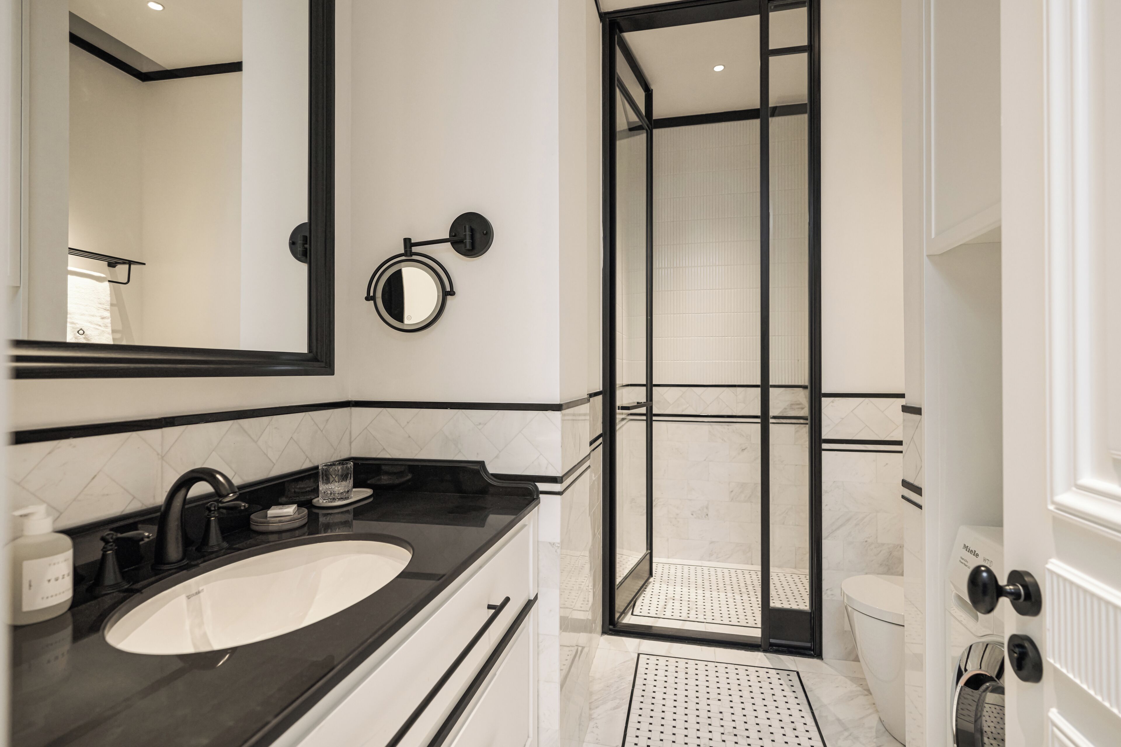 Un bagno moderno con uno specchio grande, un lavabo su piano nero e una cabina doccia in vetro.