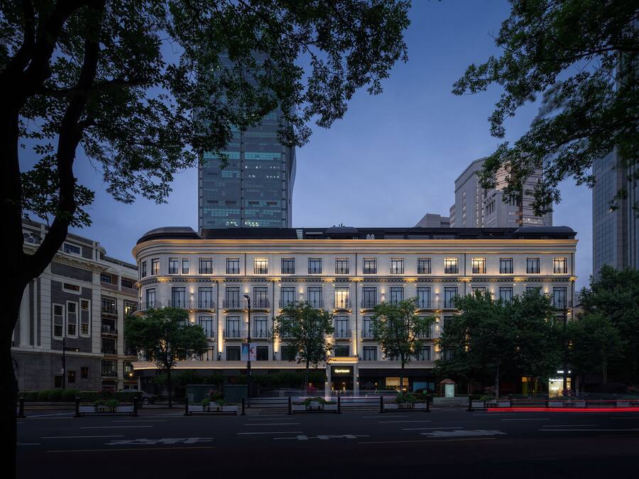 A multi-story hotel with a classic architectural design, featuring a central courtyard and a modern building in the background.