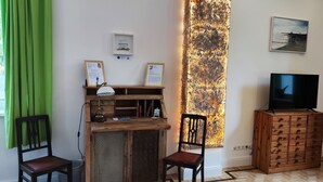 Una habitación con un escritorio de madera, dos sillas, un televisor sobre un mueble de madera y un cuadro abstracto grande en la pared.