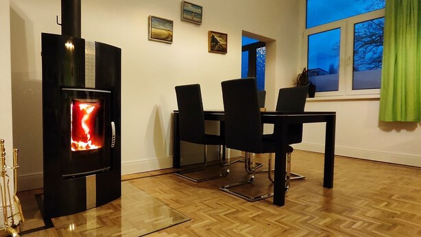 Una habitación con estufa de leña, una mesa de comedor con sillas y una ventana con vistas al exterior.