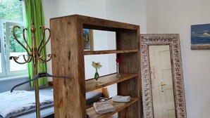 Una habitación con una estantería de madera, un espejo con marco decorativo, un cuadro en la pared y una ventana con cortinas verdes.