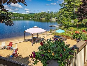 Un patio junto al lago con mobiliario exterior, una zona cubierta y vistas al lago y la vegetación circundante.