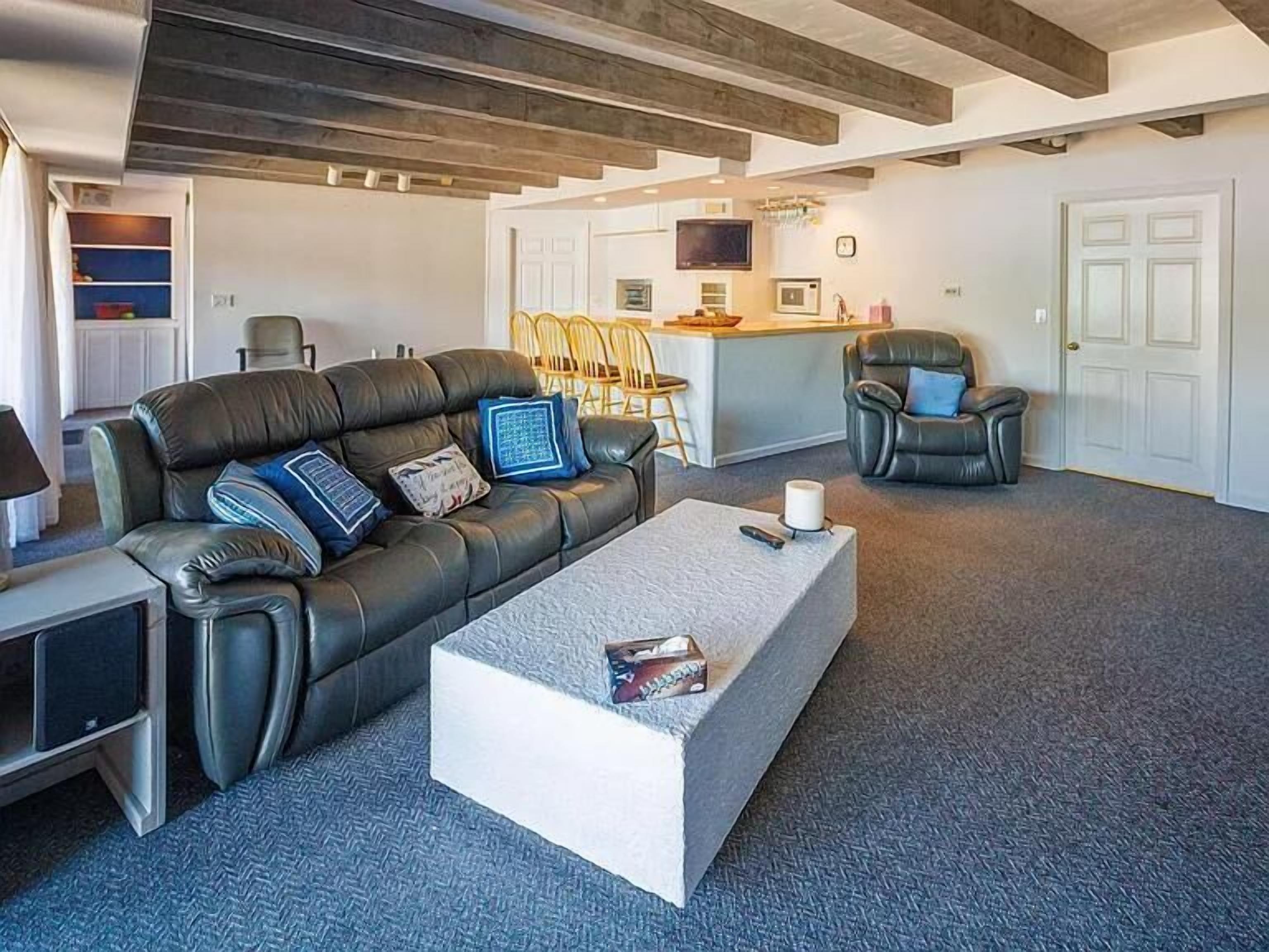 A modern living room with a leather sofa, a white coffee table, and a kitchen area in the background.