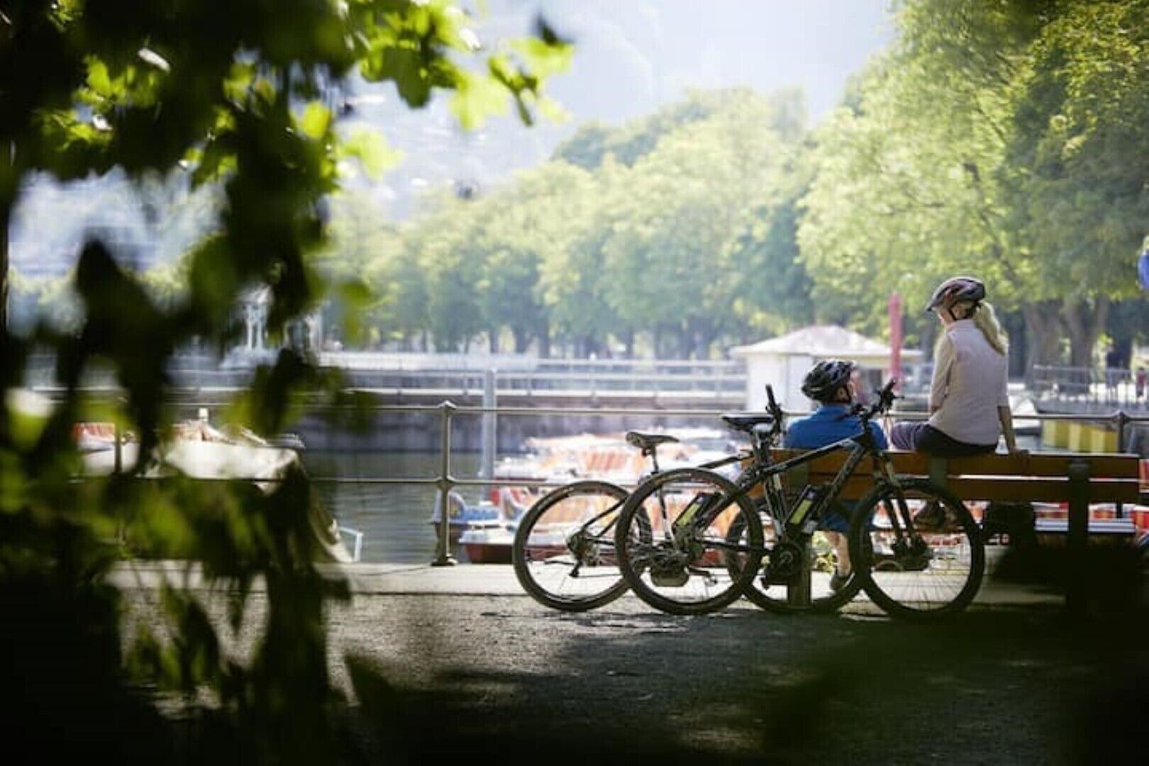 Een park met een bank en fietsen, met uitzicht op een waterpartij met boten.