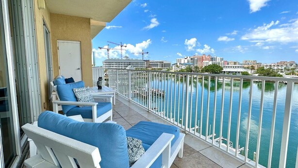 Un balcon avec des fauteuils bleus dotés de coussins et une petite table, d’où l’on peut admirer un plan d’eau avec une vue sur la ville en arrière-plan.