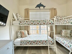 Une chambre avec un lit superposé, une literie à motifs floraux, une décoration murale représentant un dauphin et une fenêtre avec des rideaux.