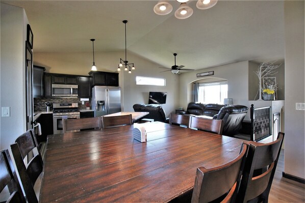 A spacious dining area with a large wooden table and modern kitchen in the background.