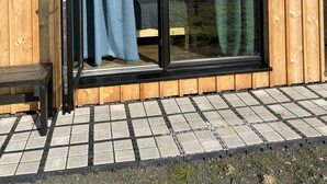 Une cabane en bois dotée d’une porte-fenêtre coulissante, d’un petit espace extérieur aménagé pour s’asseoir et offrant une vue sur un champ verdoyant.