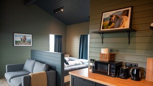 Une pièce chaleureuse avec un canapé gris, un lit avec des rideaux bleus, un comptoir de cuisine en bois équipé d’appareils électroménagers et, au mur, un tableau encadré représentant un cheval.