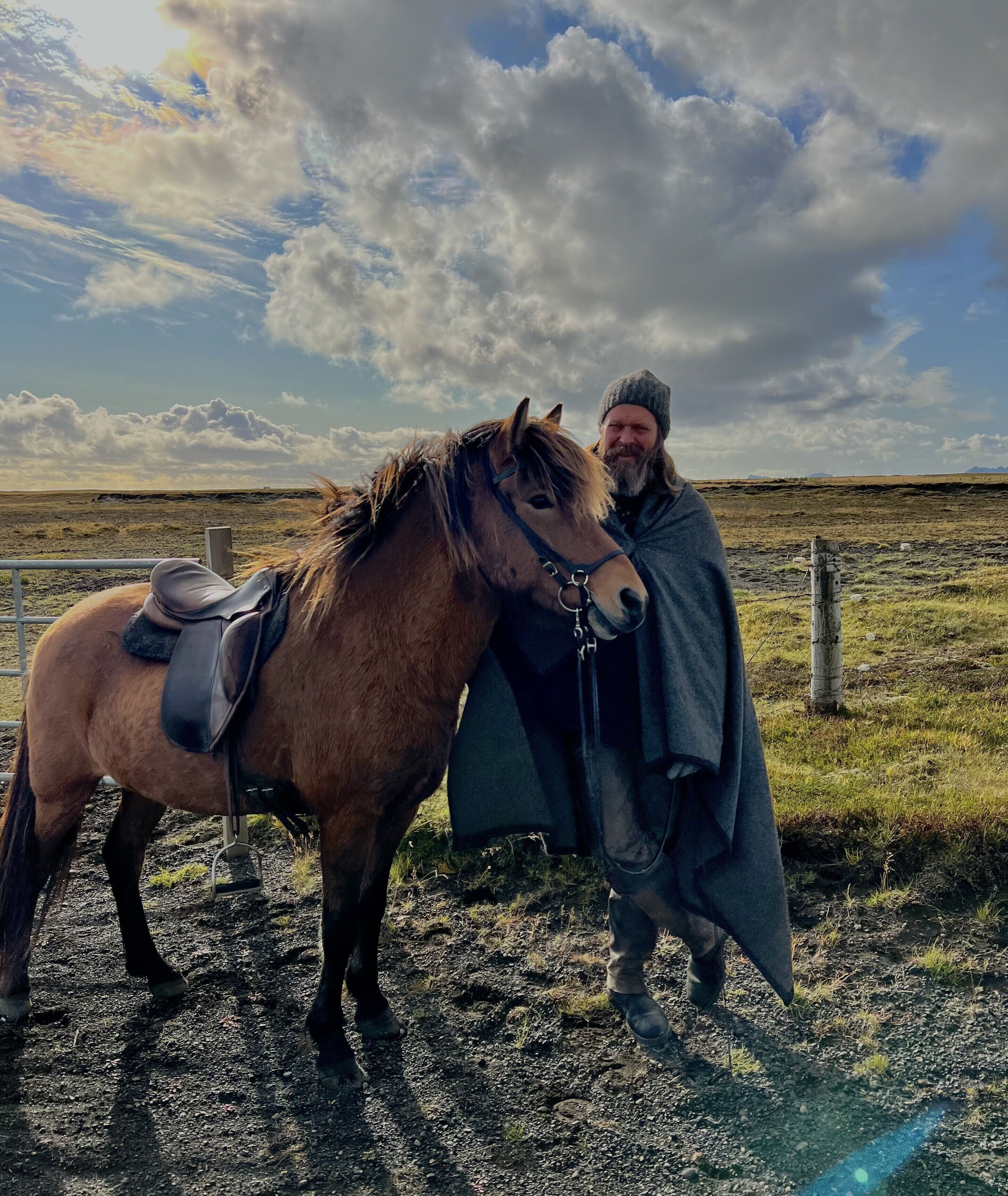 A person standing next to a horse in an open field with a fence in the background.