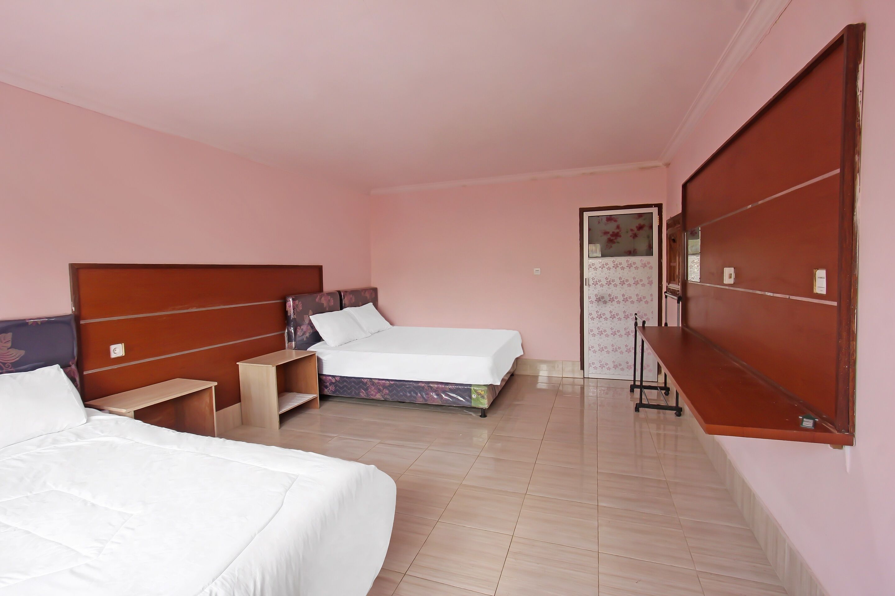 A hotel room with two beds, a wooden headboard, a small wooden table, a mirror, and a wardrobe.