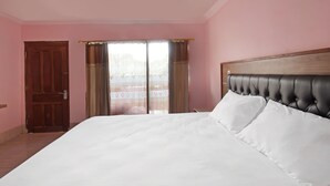 Un grand lit avec du linge de lit blanc, dans une pièce aux murs roses et dotée d’une tête de lit en bois.