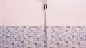Une douche équipée d’un pommeau de douche à main et d’un flexible, installée devant un mur carrelé à motifs à carreaux.