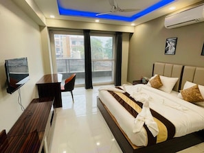 A modern hotel room with a bed, a desk, a chair, and a TV. - Hotel Olive Saffron (New Delhi)