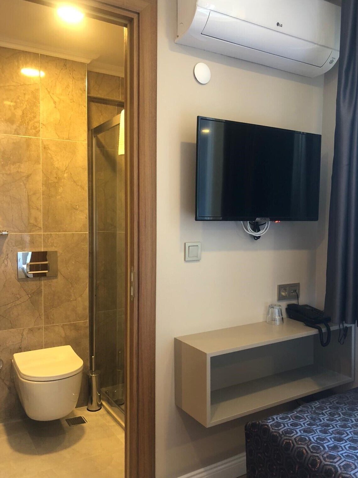 A modern bathroom with a toilet, shower, and a mounted flat-screen TV.