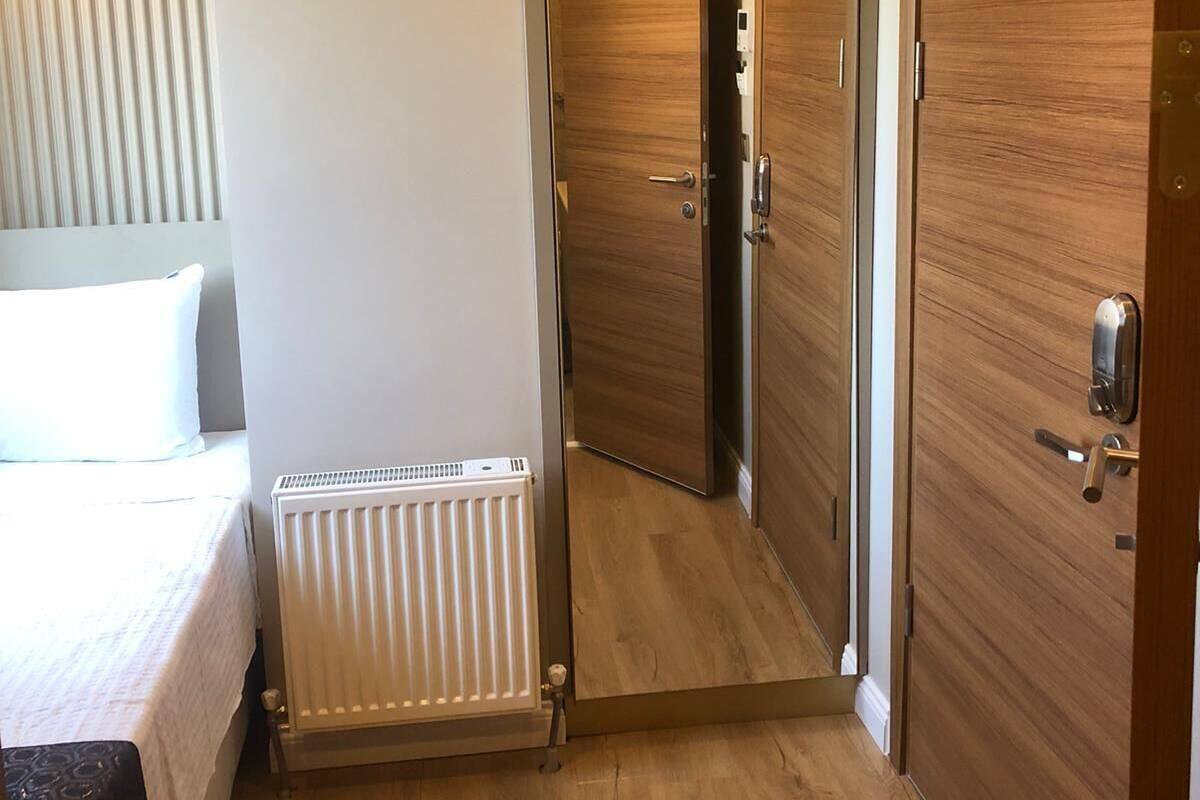 Una habitación de hotel con cama, radiador, puertas de madera y un pasillo.