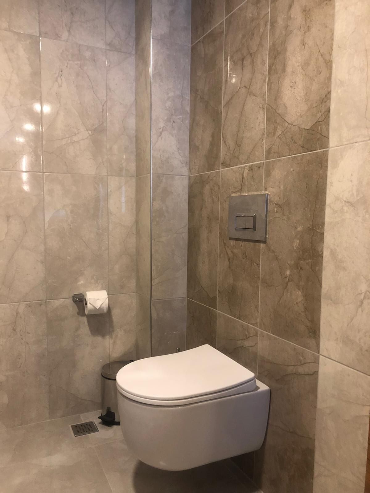 A bathroom with a white toilet, a marble-tiled wall, and a visible electrical outlet.
