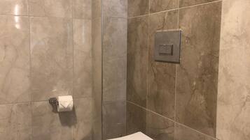 A bathroom with a white toilet, a marble-tiled wall, and a visible electrical outlet.