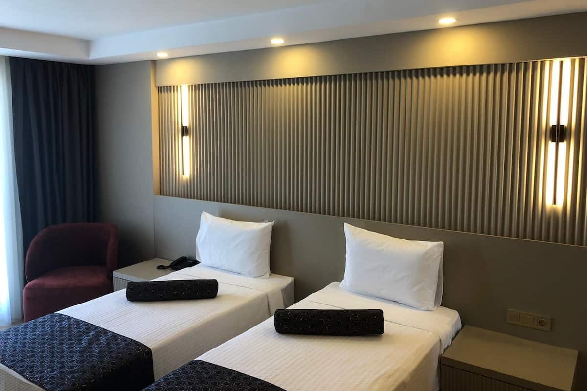 Habitación de hotel con dos camas, un escritorio, una silla y una lámpara fijada a la pared.