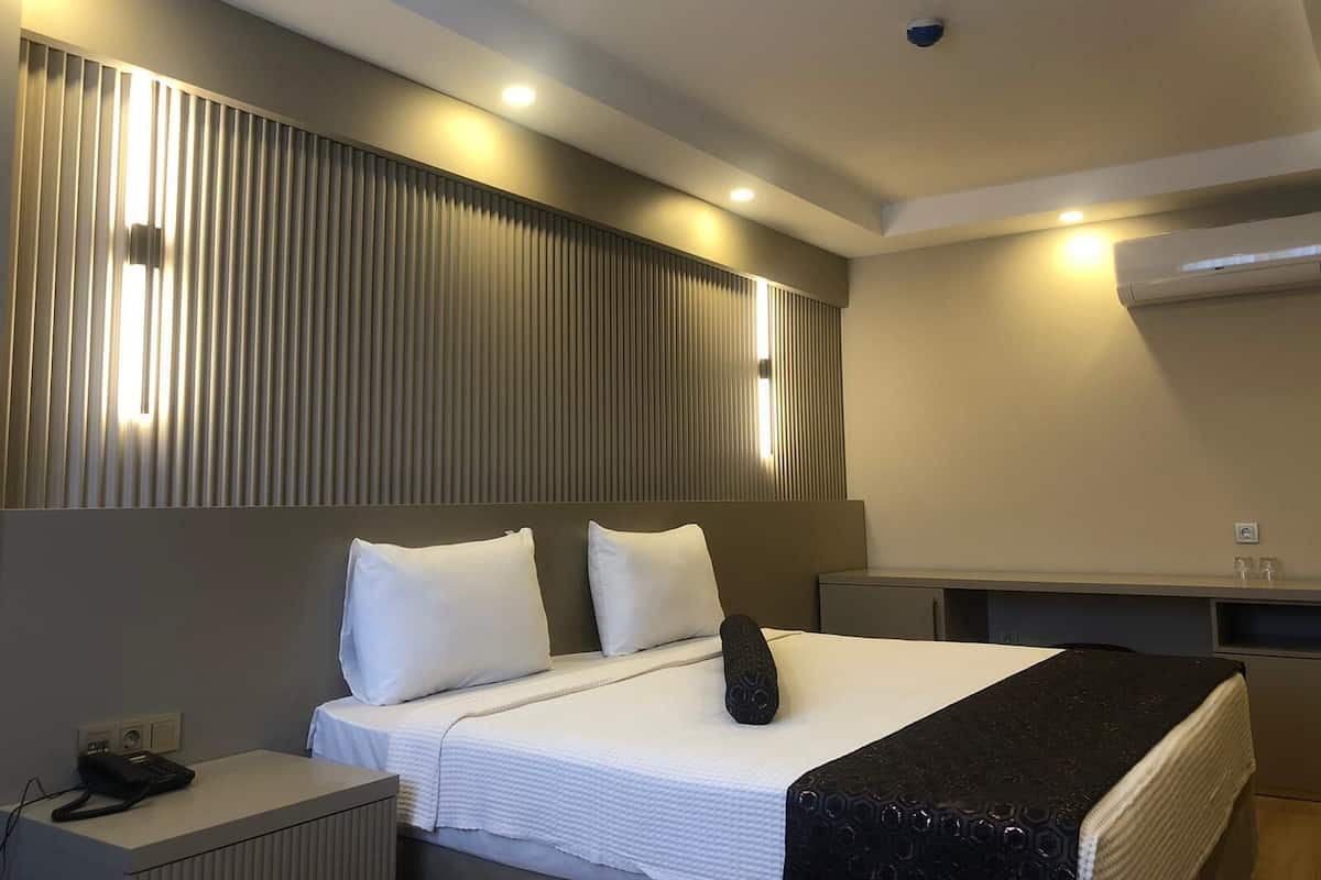 Una habitación de hotel con una cama grande, una mesita de noche, un escritorio y aire acondicionado instalado en la pared.