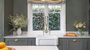 A kitchen with a double sink, a window with a view of pink flowers, and a vase with pink flowers on the counter. - Werona Cottage – enchanting home (Burrawang)