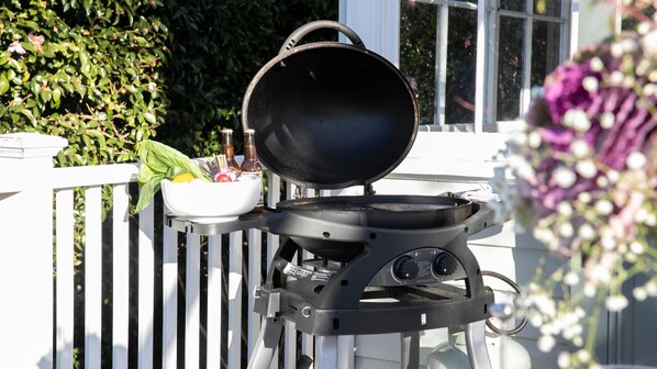 A portable grill with a lid open, placed on a white deck.