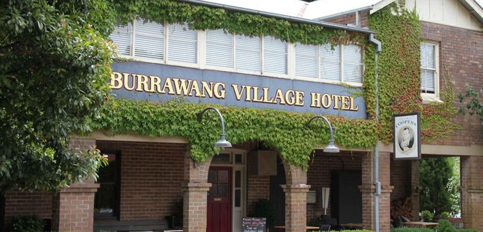 La façade de l’hôtel Burrawang Village, avec ses murs recouverts de lierre et une enseigne bien visible.