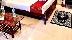 A hotel room with a bed, a wooden side table, a red and white bedspread, and a decorative rug. - HOTEL SITA GRAND (Hyderabad)